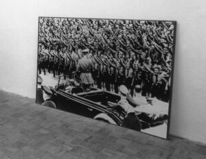 Ein Foto, an die Wand gelehnt, zeigt Adolf Hitler vor einer Menge junger Männer in Uniform mit Hitlergruß.
