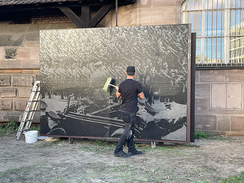The poster installer smooths the print with a brush. The motif shows Adolf Hitler in front of a crowd of young people in Hitler Youth uniforms giving the Nazi salute.